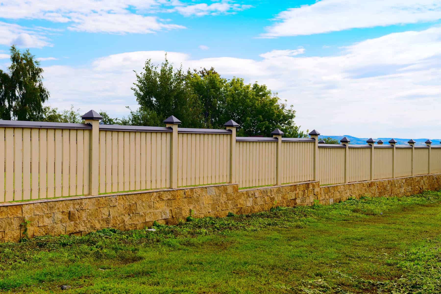 Cream Metal Fence Painting Cream-painted metal corrugated fence with black caps and stone base in residential setting.