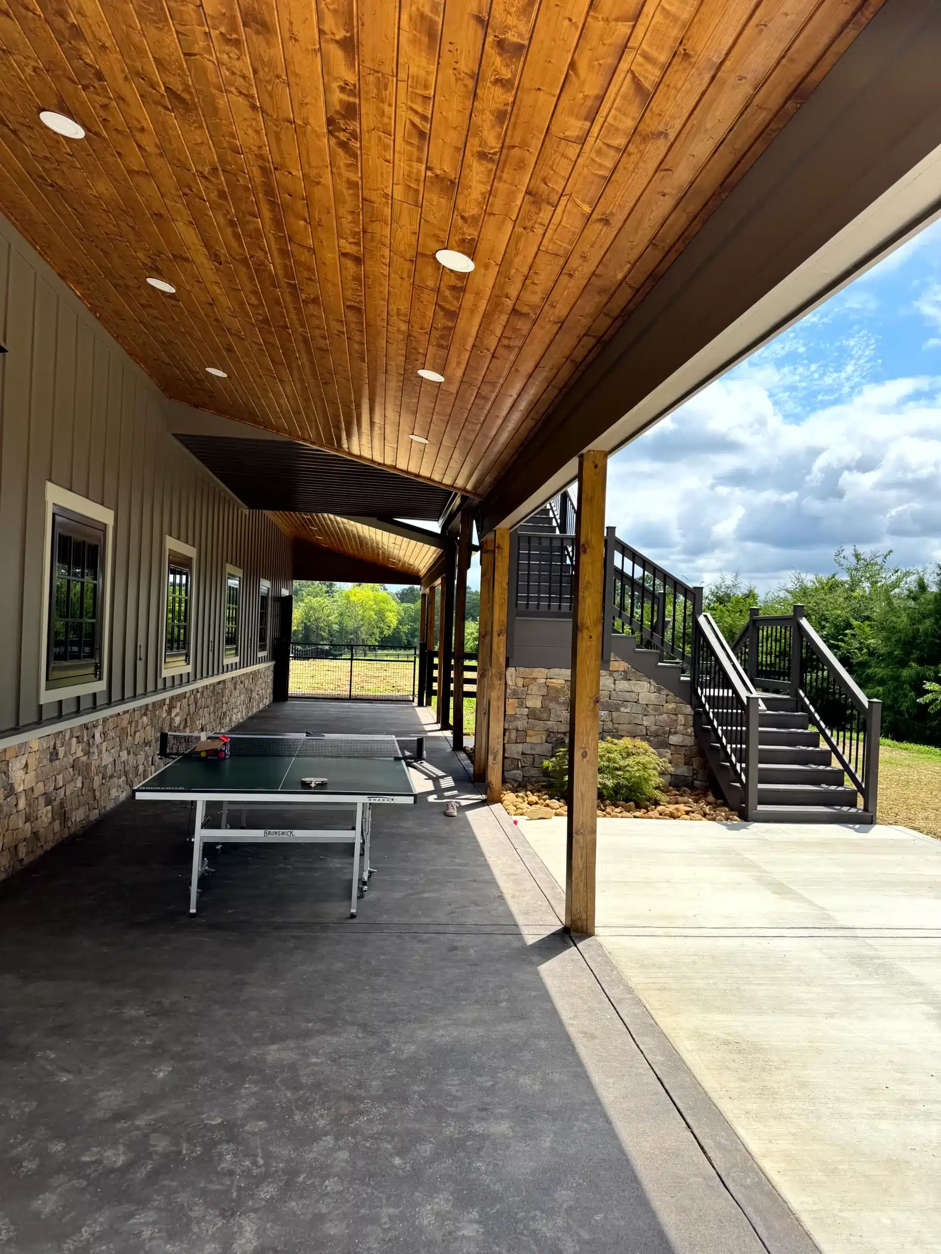 Cedar Ceiling Covered Patio Golden-stained cedar plank ceiling on covered patio with recessed lighting, stone accent wall, and concrete floor.