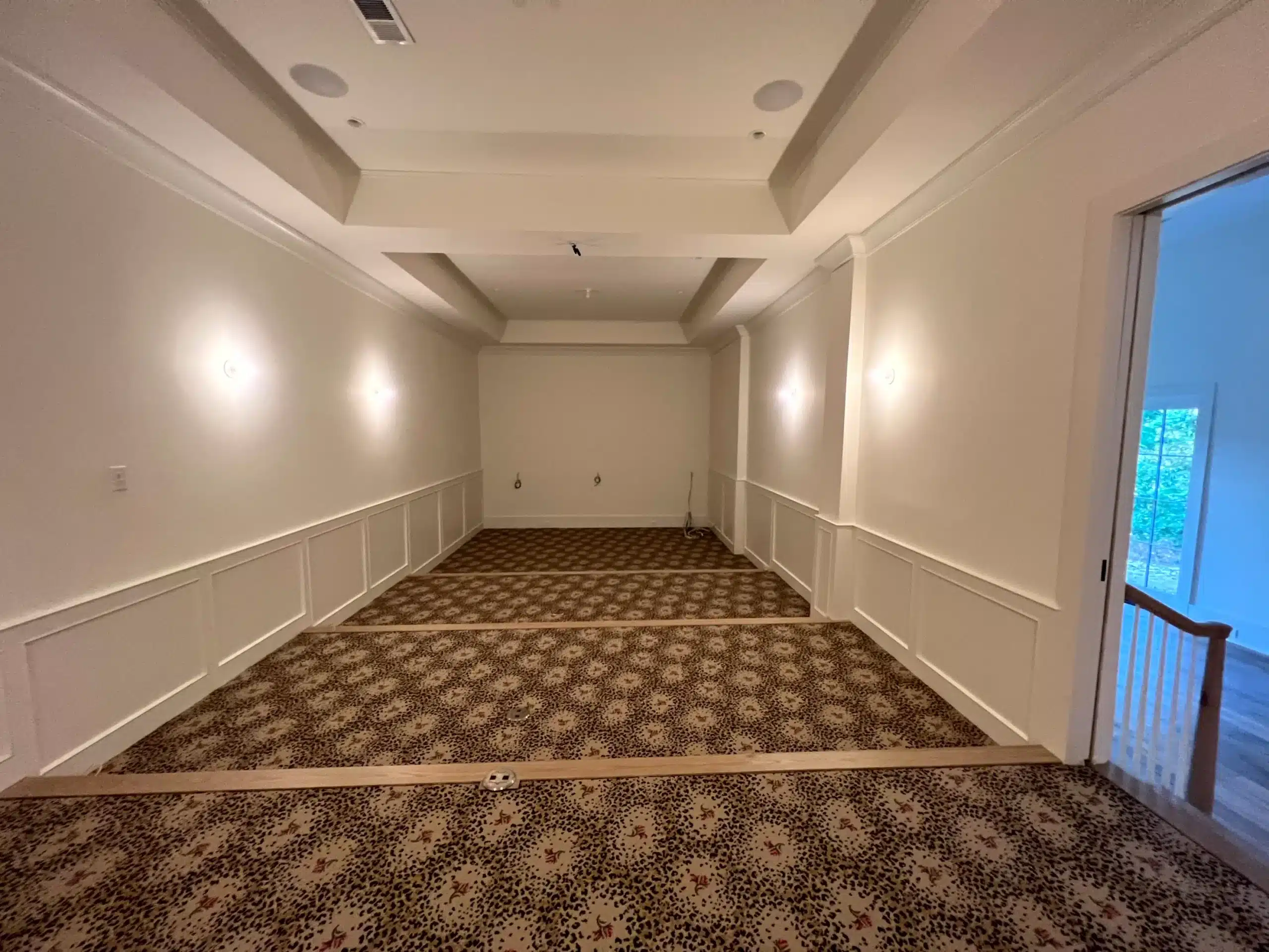 Cream Interior Room With Wainscoting Cream-painted interior room with white wainscot paneling, coffered ceiling, recessed lighting, and patterned carpet flooring.