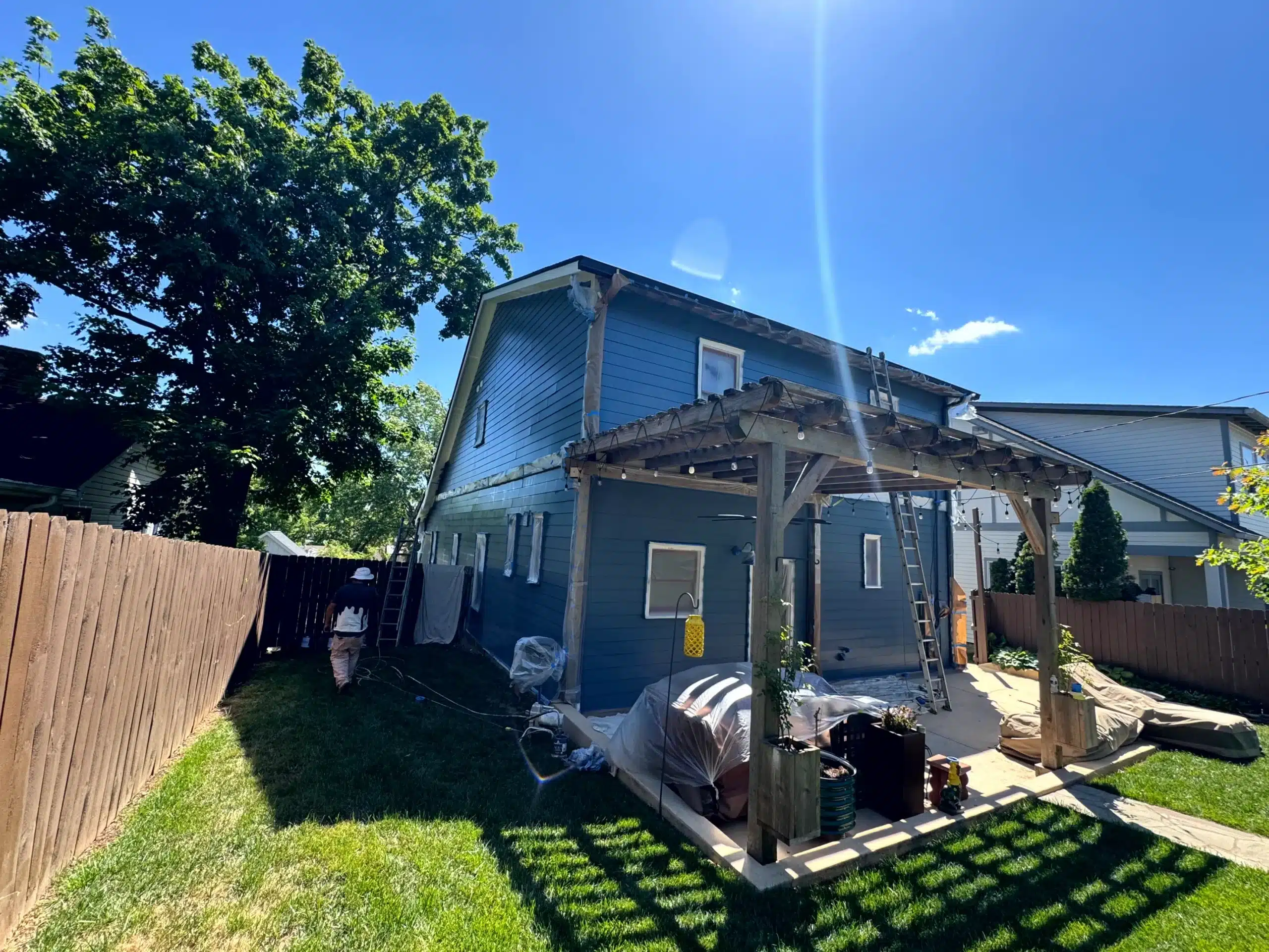 Navy Blue Residential Home Exterior Navy blue painted residential home with white trim, wooden pergola, and protective sheeting during exterior painting project