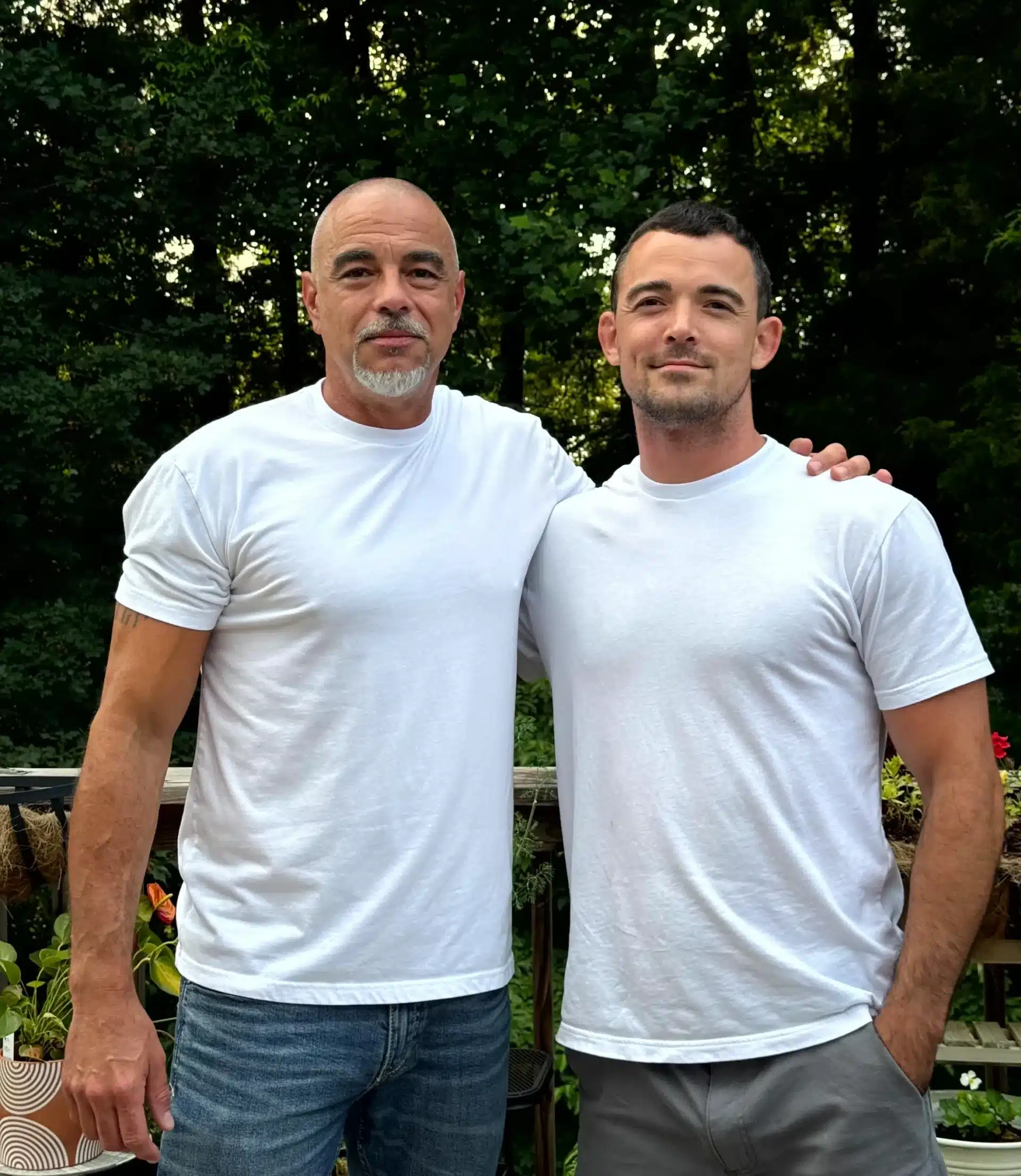 Painting Company Team Portrait Two men in white t-shirts standing together outdoors with green foliage background.