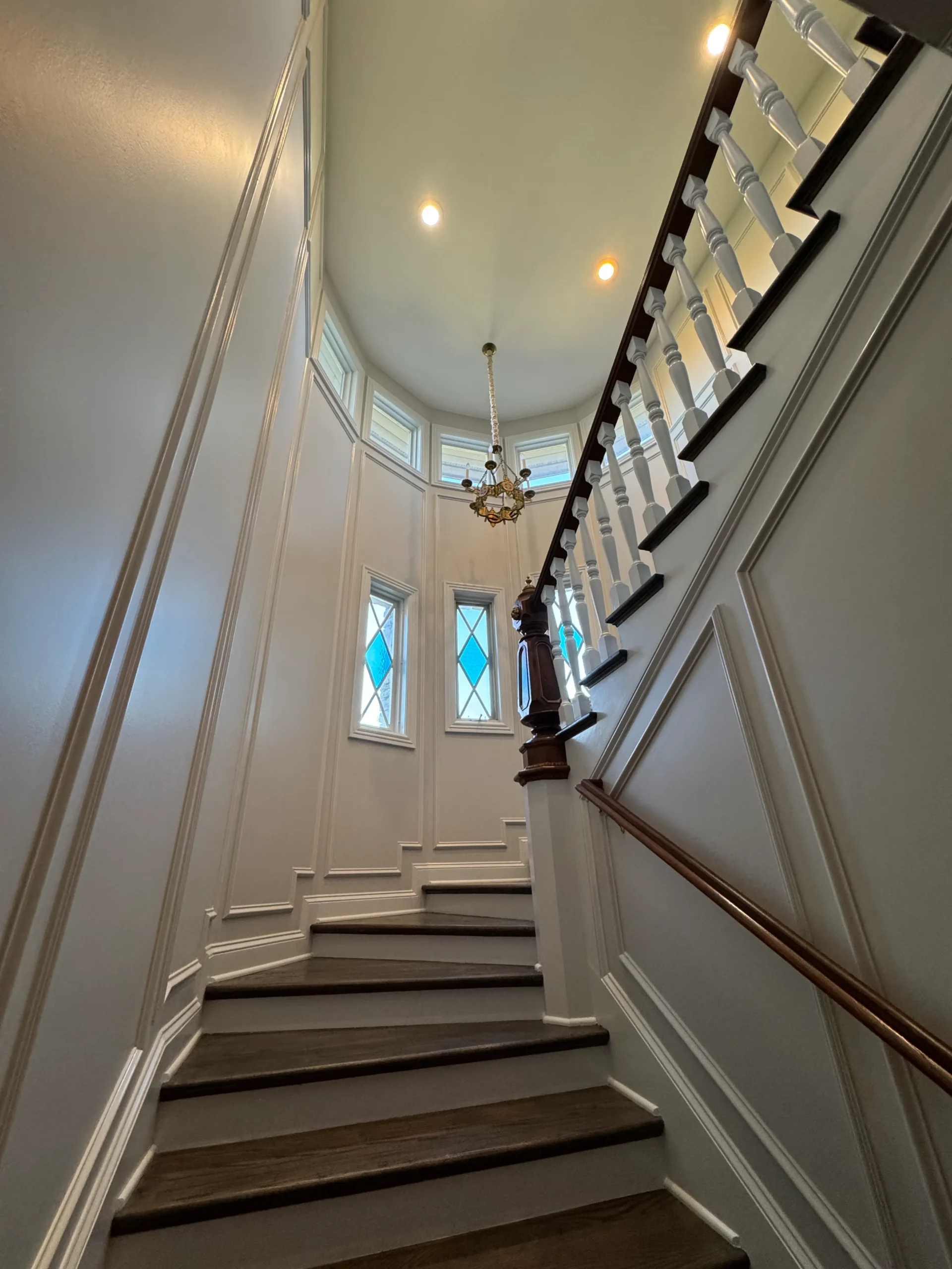 Cream Painted Stairwell With Dark Wood Steps Cream-painted residential stairwell with dark wood treads, white wainscoting, dark wood handrail, and arched ceiling with