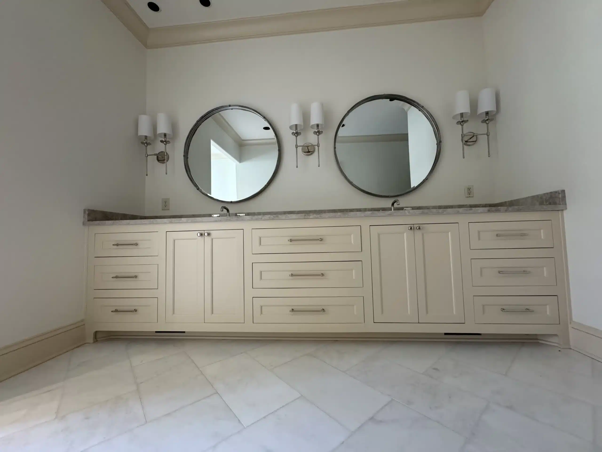 Cream Painted Bathroom Vanity Cream-painted double bathroom vanity with recessed panel cabinetry, brushed metal hardware, and round mirrors with sconces