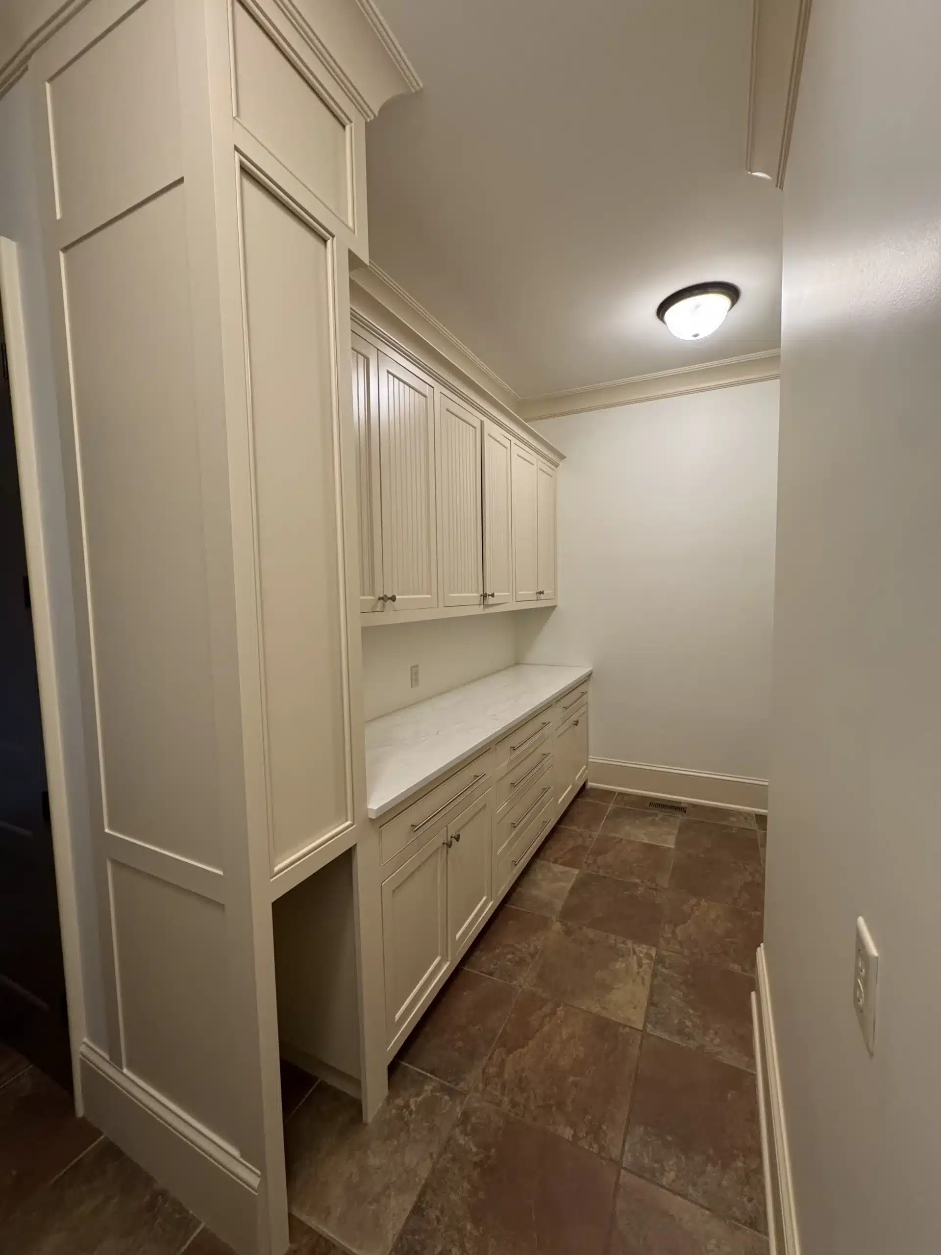 Cream Painted Laundry Room Cabinetry Cream-painted laundry room cabinetry with recessed panels, upper and lower cabinets, white countertop, and brown tile