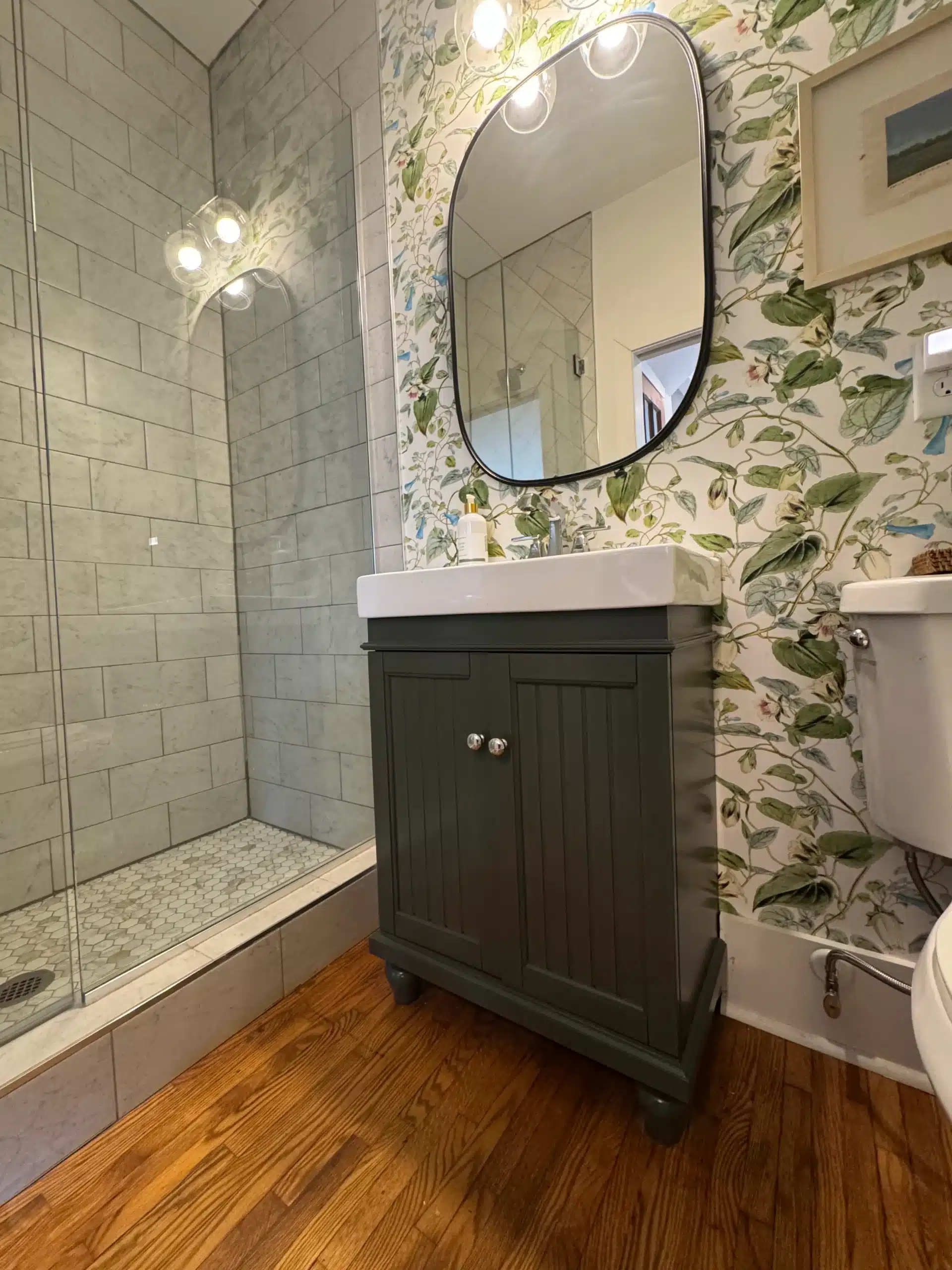 Black Painted Bathroom Vanity Cabinet Black-painted bathroom vanity with white countertop, round mirror, and recessed panel cabinetry doors in residential bathroom