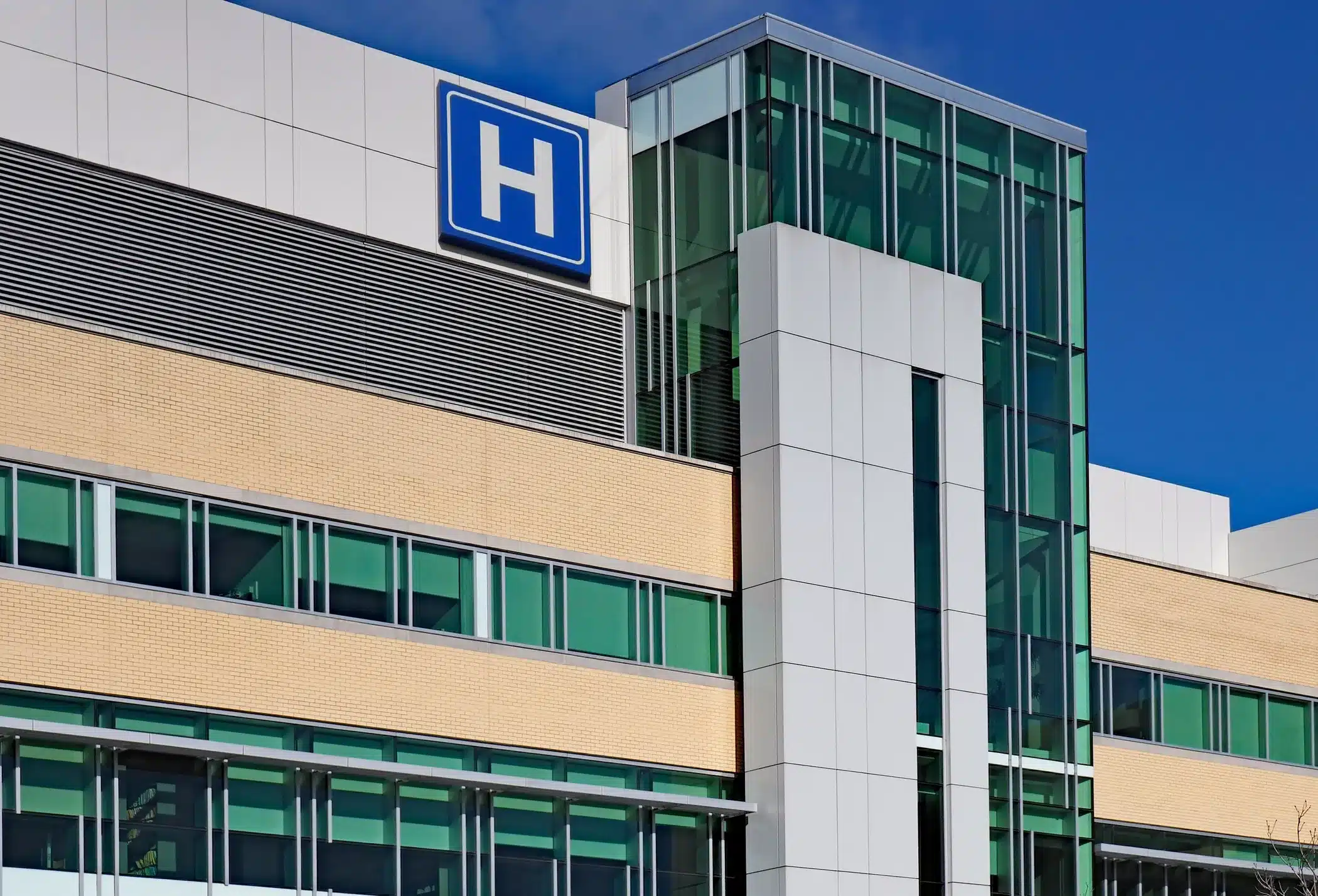 Modern Hospital Building Exterior Modern commercial hospital building with white panel facade, cream brick banding, green-tinted windows, and blue hospital H